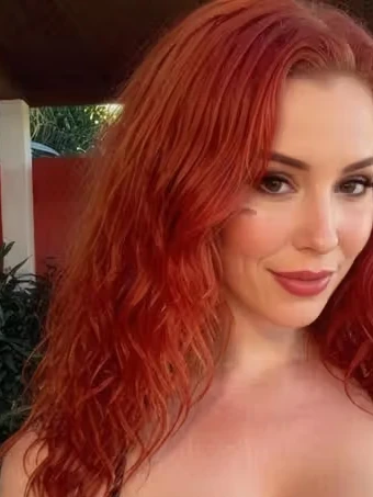 Porträt von Jessica, einer KI-Figur des Anbieters GoLove: rote Locken, geblümtes Oberteil, draußen im Sonnenlicht.